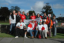 A group of thirteen supporters pose together, some wearing rugby jerseys while others sport traditional Japanese costumes and Japanese flags.