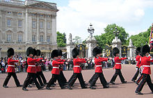 Líneas de hombres vestidos con grandes sombreros de piel de oso negro y túnicas de color rojo.